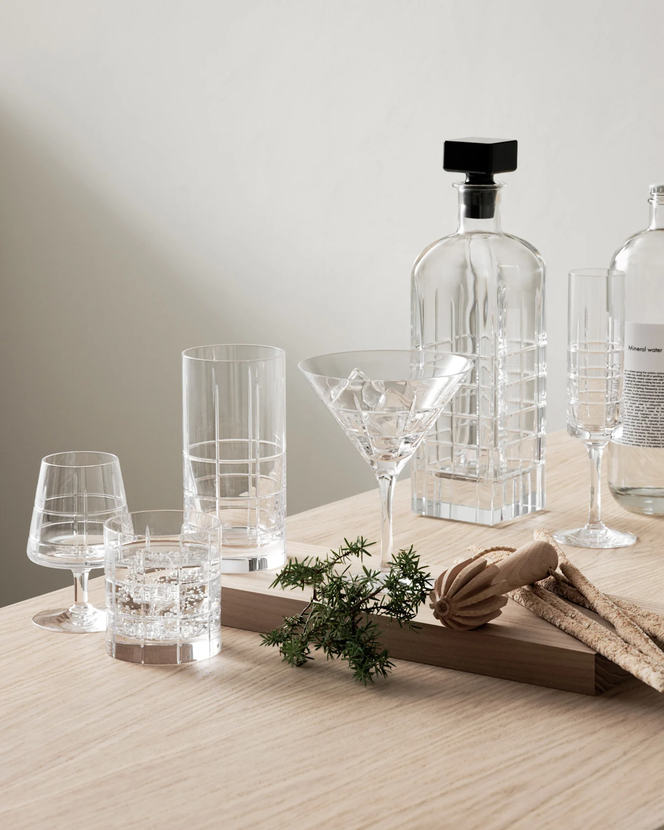 Klar glas karaffel, mønstrede glas, mineralvandsflaske med enebær og grissini på træbord.