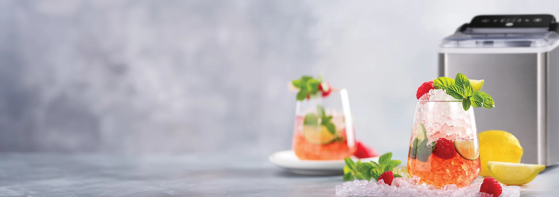 Forfriskende hindbærdrikke med knust is, mynte, lime, ved siden af en ismaskine og friske citroner.