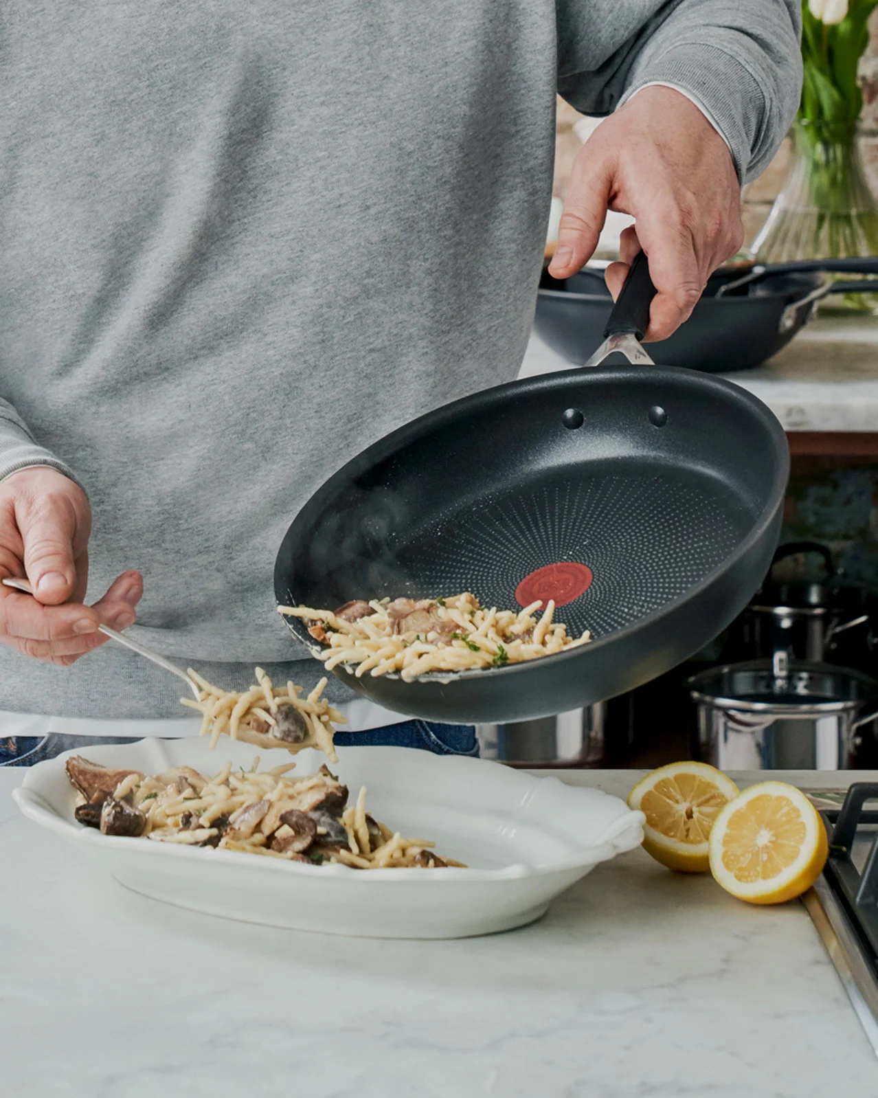 Person der serverer pasta med svampe fra en pande til en serveringsskål.